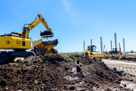 Big excavator is filling a dumper truck with soil at construction site, project in progress.