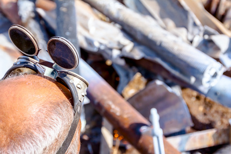 Worker is cutting scrap metal with acetylene torch wearing protective goggles on his head.の写真素材