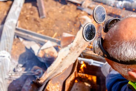 Worker is cutting scrap metal with acetylene torch wearing protective goggles on his head.