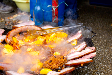 Delicious potatoes, bacon and juicy sausages made of minced meat are simmering on barbecue.の写真素材
