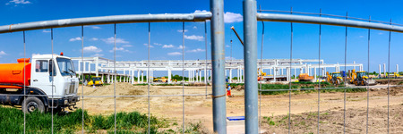 Panorama is taken with wide lens, unfinished concrete edifice under construction, people are working with machinery.の写真素材