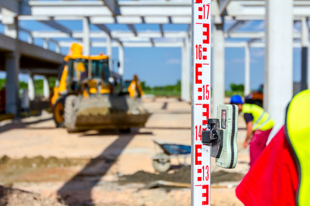Construction worker is holding leveling rod to help surveyor, geodesist to measure position, depth.