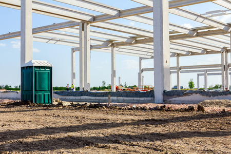 Concrete skeleton of unfinished new edifice and public lavatory for workers is placed at...