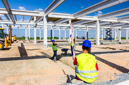 Construction worker is holding leveling rod to help surveyor, geodesist to measure position, depth.