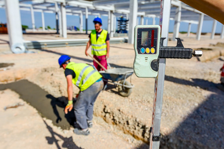Construction worker is holding leveling rod to help surveyor, geodesist to measure position, depth.