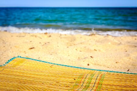 Straw mat is placed on the sandy beach close to wavy sea.