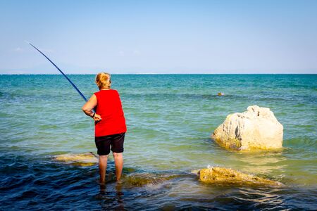 Senior woman is standing in the sea and fishing.の写真素材