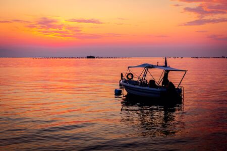 Silhouetted shot of beautiful sunrise with fisherman boat on the waterの写真素材