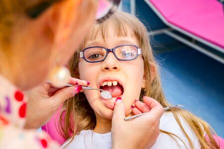 Portrait of sweet little girl with open mouth, glasses and carefree expression on her face during the dental check.の写真素材