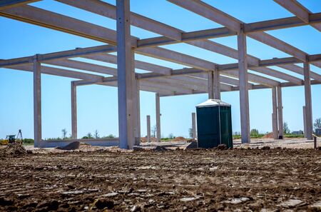 Concrete skeleton of unfinished new edifice and public lavatory for workers is placed at...