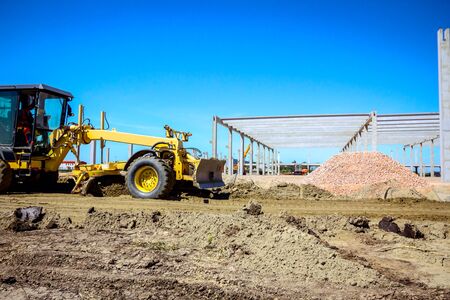 Operator is driving yellow grader, leveling ground at building site.
