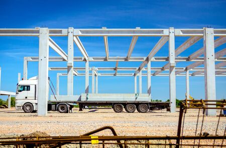 Truck with trailer is transporting long and heavy concrete beam to construction site for industrial edifice.の写真素材