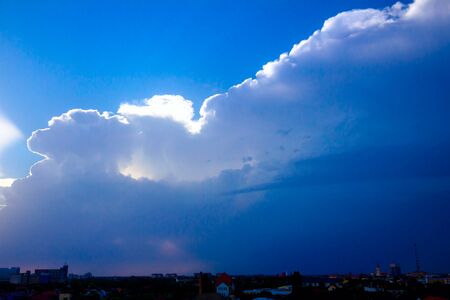 View of sunlight rays from cumulus clouds on turquoise sky and the silhouette of city in distance.の写真素材