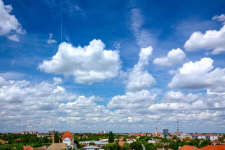 Scenic view is on beautiful blue sky with white fluffy clouds and cityscape in the distance.の写真素材