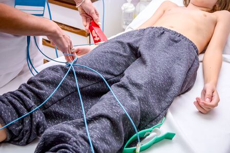 Cardiologist is attaching vacuum sensors to child, teenager patient for recording ECG or EKG...