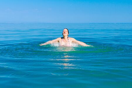 Restless beautiful cheerfully woman is having fun and jumping out with widespread hands in sea water...