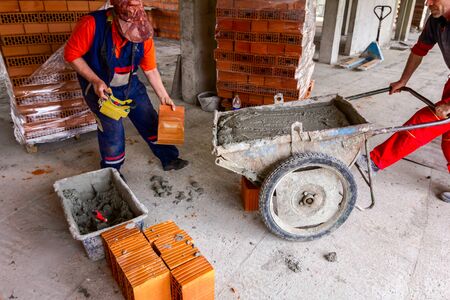 Construction workers are using their manpower to manage wheelbarrow with fresh mortar at...