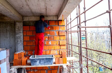 Mason, bricklayer worker is using red blocks to mount a wall at construction site.の写真素材