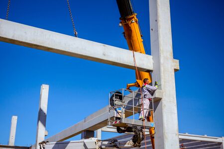 Mobile crane is operating and worker is assembly concrete joist in high place. Height worker is...