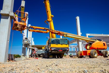 Mobile crane is operating and worker is assembly concrete joist in high place. Height worker is...