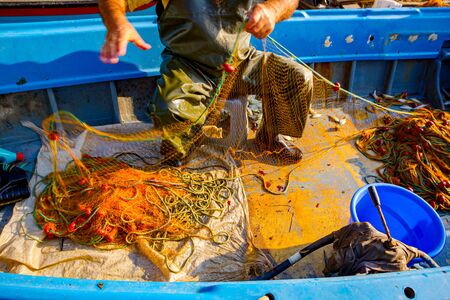 Fisher in rubber trousers and boot siting in his boat and pile up fishing net for angling at open sea.の写真素材