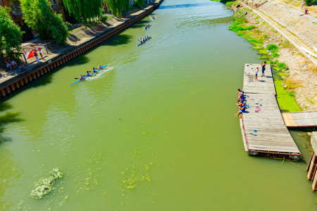 Young rowers have a competition in kayaking on the river, children sit on the wooden planks and watch the race.のeditorial素材