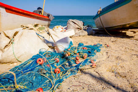 Packed heap of fishing net is on the sandy beach between fishing boats.