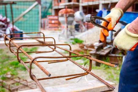 Worker is tying rebar with wire using pliers, to make a reinforcing frame for concrete beam.