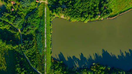 Above view over embankment, dam of lake at hilly landscape, woodland, rural road.