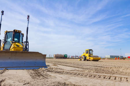 Vibration plate compactor is mounted to the steamroller, compacting sand at road construction site.