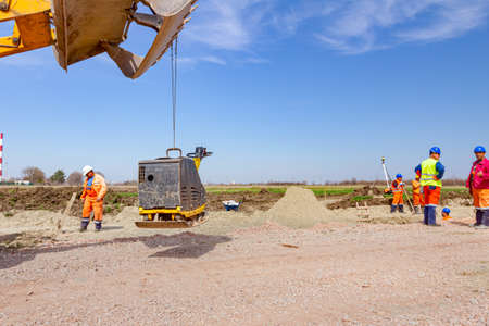 Excavator is carry, over building site with raised up front bucket, vibration plate compactor...