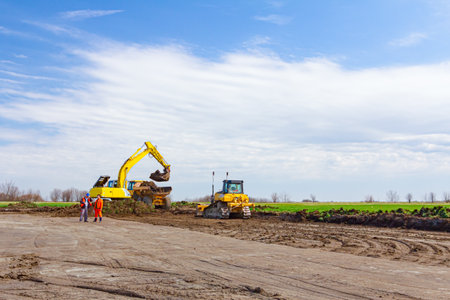 Project is in progress, excavator is filling a dumper truck with soil and road roller is flatting,...