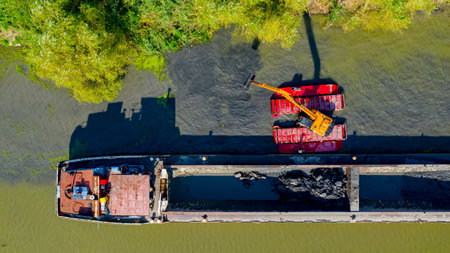 Above top view on excavator dredge is dredging, working on river, canal, deepening and removing sediment, mud from riverbed in a polluted waterway.の写真素材