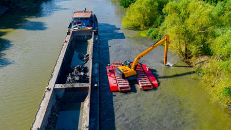 Above view on excavator dredge is dredging, working on river, canal, deepening and removing sediment, mud from riverbed in a polluted waterway.の写真素材