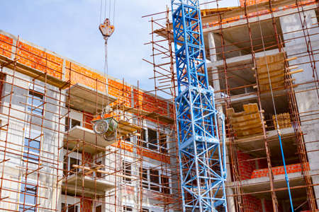 Crane is carry wheelbarrow, been pulled up on ropes above building site.の写真素材