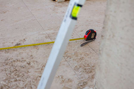Spirit level placed next to the wall and metal measure tape is on the concrete floor after usage for construction site for measurement and control.の写真素材