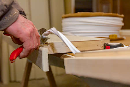 Carpentry worker is holding red metal pliers and cutting rubber tape that is putted in wooden door...