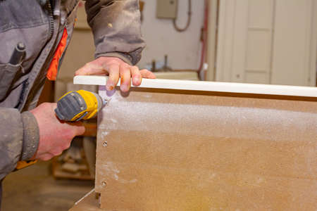 Worker in carpentry uses professional manual power tool, acu drill, and twists the screws on the...