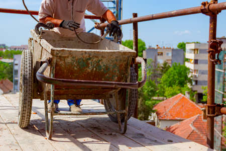 Construction worker is attaching crane hooks to industrial tipping barrow.の写真素材