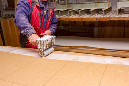 Carpentry worker uses handy roller tool, spreader for applying adhesive on the wooden surface...