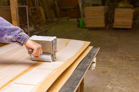 Carpentry worker uses handy roller tool, spreader for applying adhesive on the wooden surface profile, plywood that needs to be glued.の写真素材