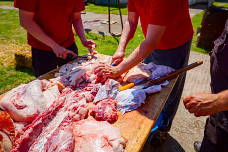 Butcher is cutting the raw pork meat into smaller pieces slice using sharp knife, prepares flesh for cooking.の写真素材