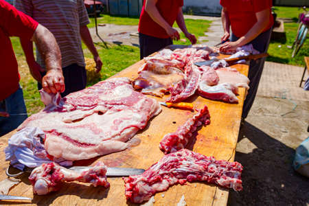 Butcher is cutting the raw pork meat into smaller pieces slice using sharp knife on a wooden board.の写真素材