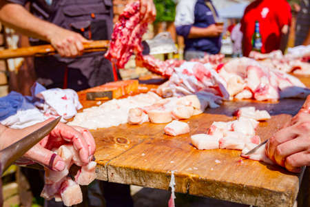 Butcher is cutting the raw pork meat into smaller pieces slice using sharp knife, prepares flesh for cooking.の写真素材