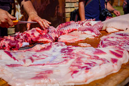 Butcher is cutting the raw pork meat into smaller pieces slice using sharp knife on a wooden board.の写真素材