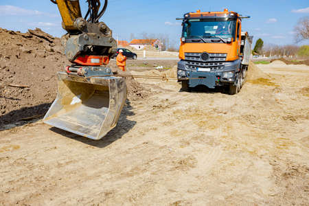 An excavator pulls a tipper truck with a cord to help him to get out from sand at building site.の写真素材