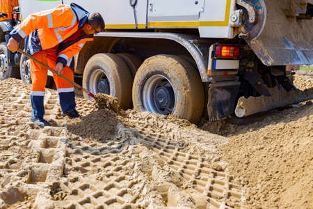 Workers are using shovels, for digging around trucks wheels, to help him to get out from sand at...