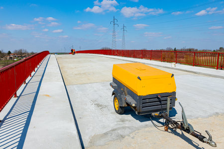 Professional yellow mobile, pneumatic compressor is parked at the bridge.