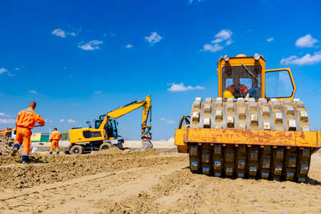 View over roller with spikes on bulldozer and excavators are leveling sand for road foundation at building site, mechanization.のeditorial素材