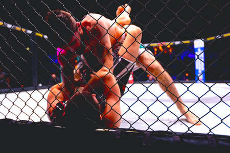 Two strong muscular professional MMA fighters fighting, they are in clinch, wrestling in parterre on octagon floor.の写真素材